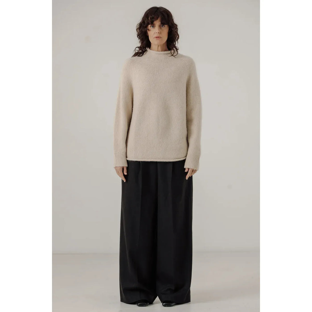 Cream women's handloom rollneck sweater by Bare Knitwear, shown draped on a model with a cozy, textured knit pattern.