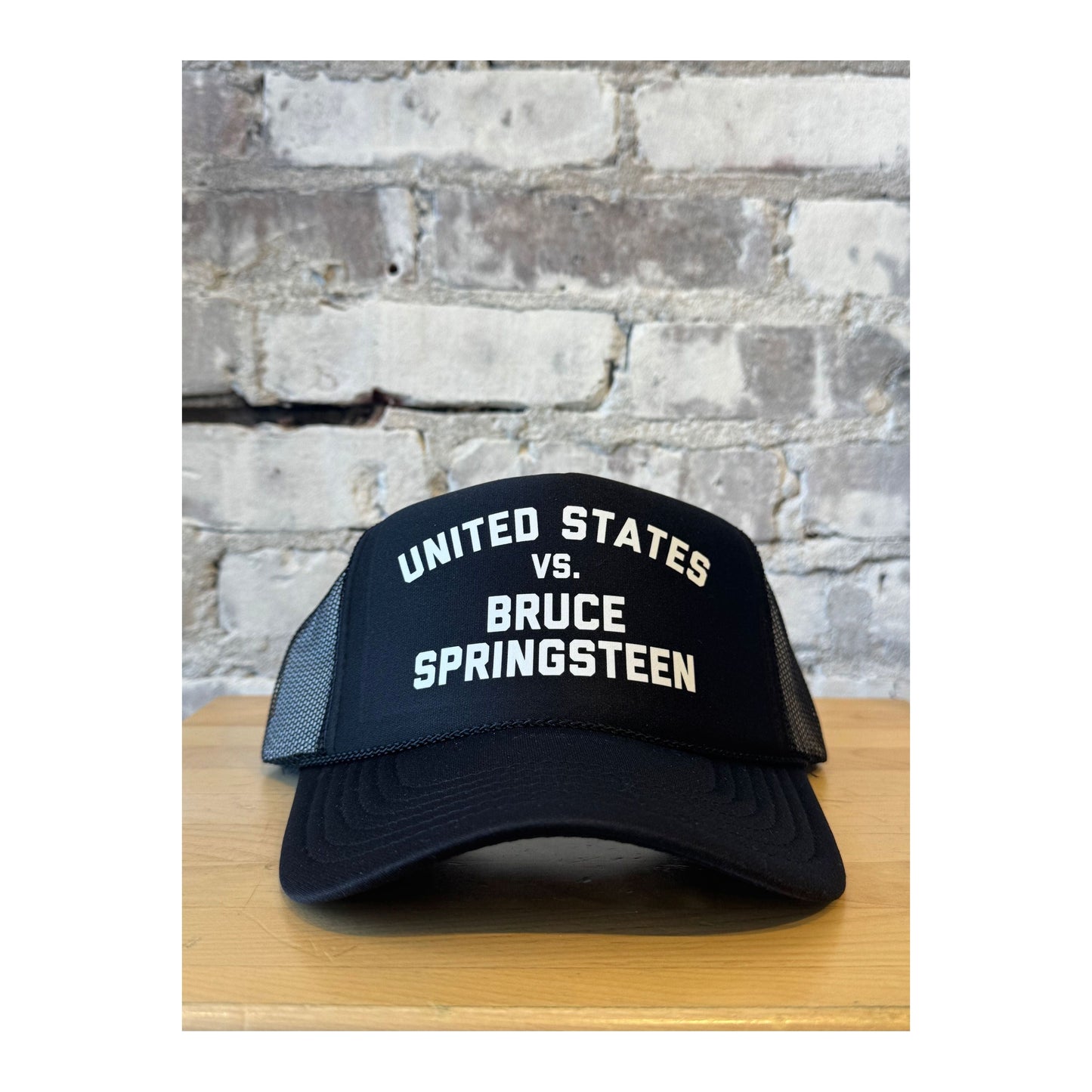 Men's black trucker hat featuring United States vs. Bruce Springsteen graphic by N.B. GOODS, with mesh back and adjustable strap.