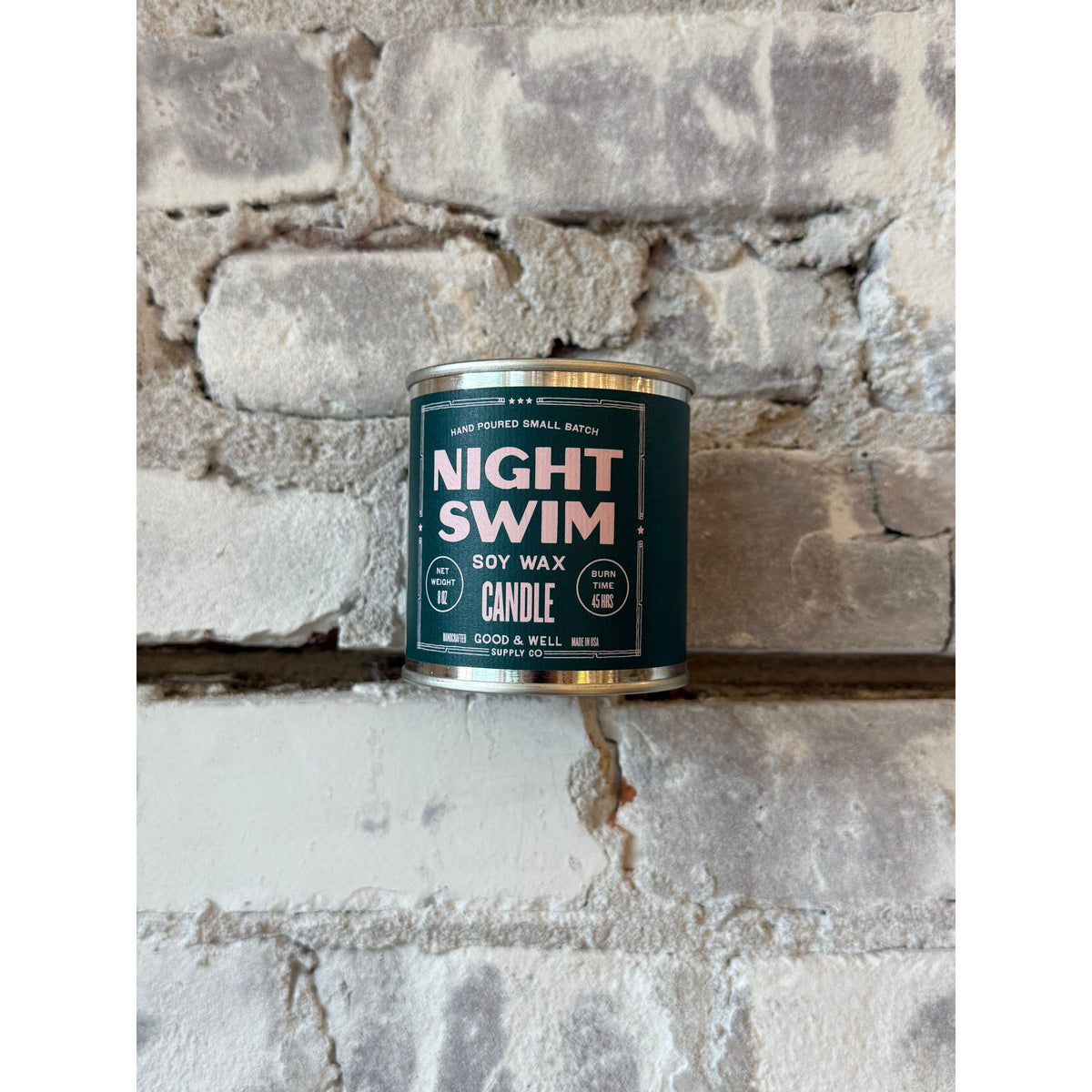 Night Swim soy candle by Good & Well Supply Co. in a glass jar, with a lit wick and a calming, dark blue label design.