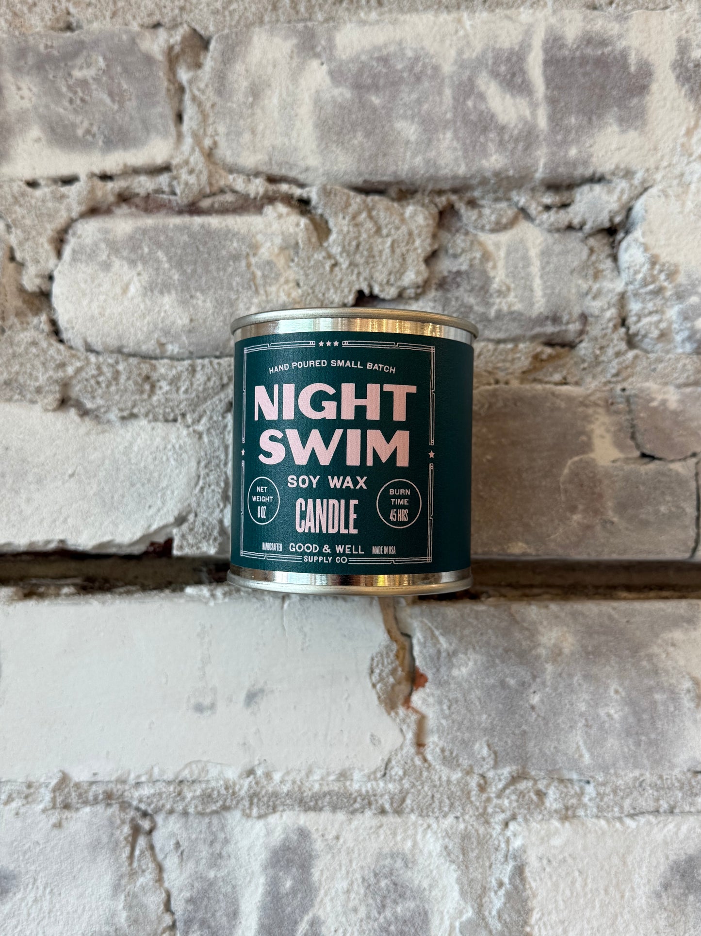 Night Swim soy candle by Good & Well Supply Co. in a glass jar, with a lit wick and a calming, dark blue label design.