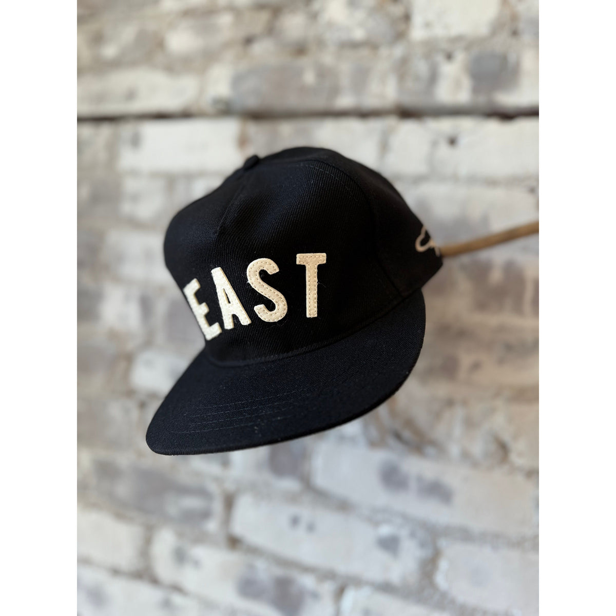 Black EAST Snapback hat by The Ampal Creative featuring a classic baseball cap style and adjustable strap.