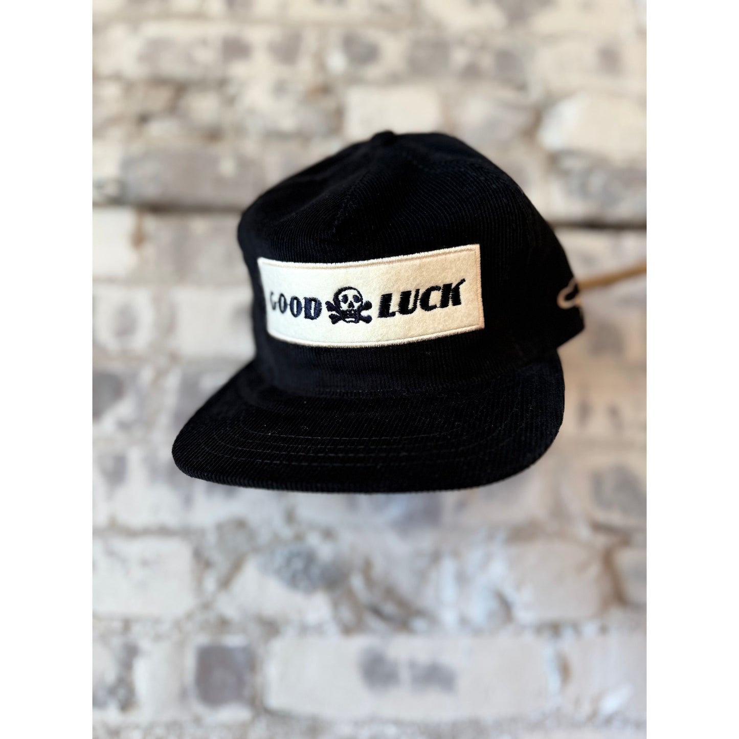Black snapback hat featuring "Good Luck" embroidery by The Ampal Creative, styled as a trendy accessory.