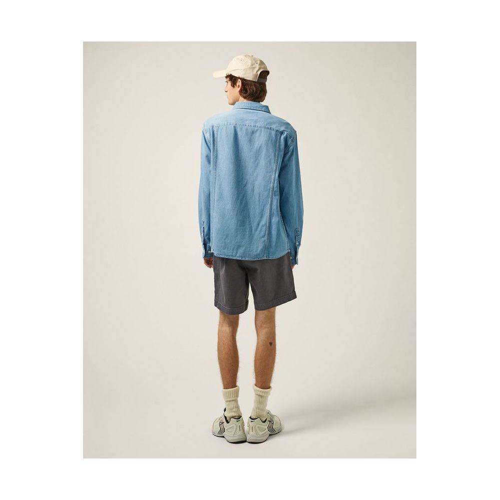 Men's light indigo denim shirt by Corridor, long-sleeve casual shirt with button front and classic fit, shown on hanger.