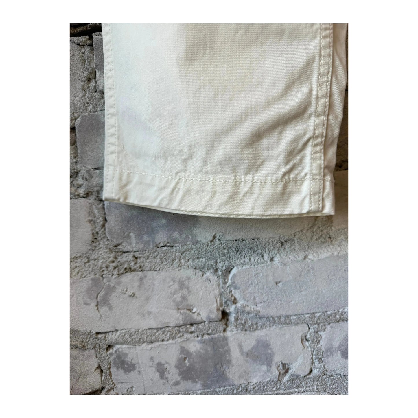 Men's off-white Cotton Chino Cloth Peg Top Pants by Sage De Cret, shown on a hanger with a close-up of fabric texture.