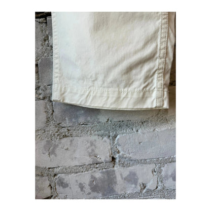 Men's off-white Cotton Chino Cloth Peg Top Pants by Sage De Cret, shown on a hanger with a close-up of fabric texture.