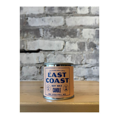 East Coast Soy Candle by Good & Well Supply Co. in a glass jar, with a lit wick and cozy ambiance.