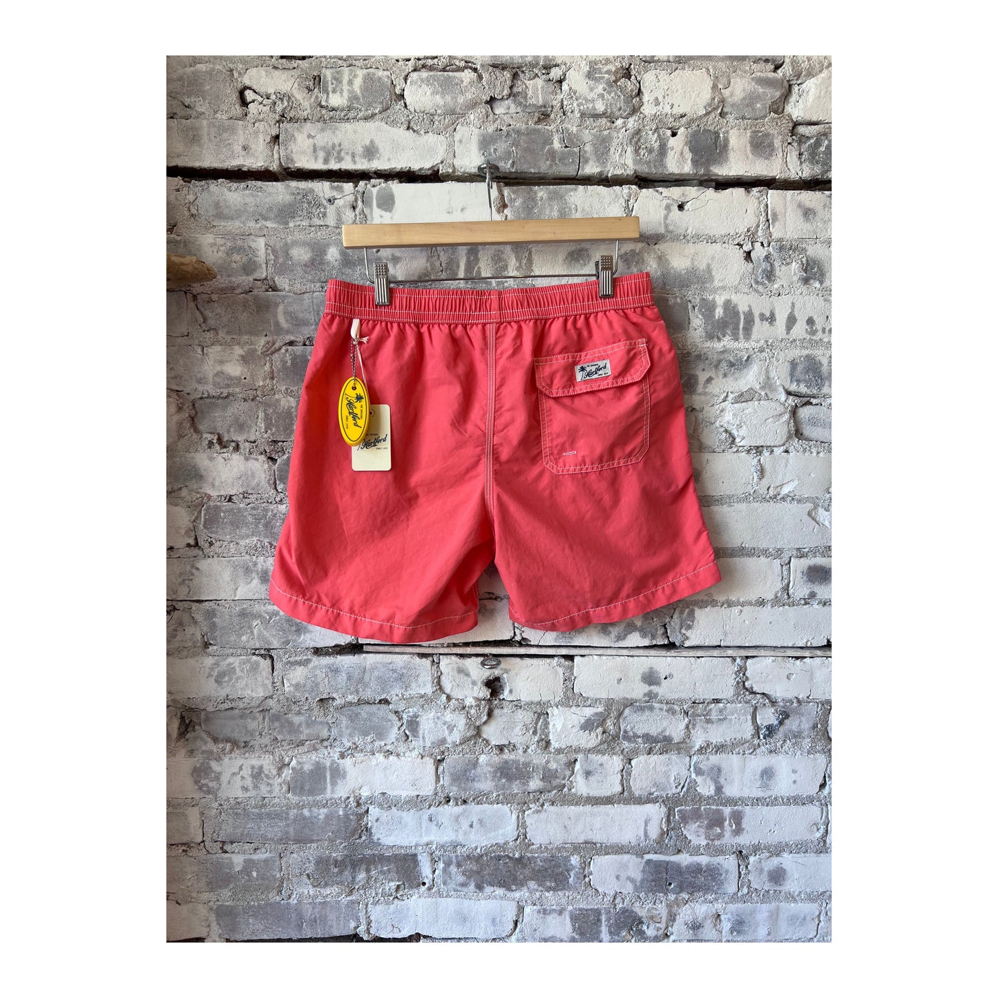 Men's Hartford Classic Swim Trunks in faded coral with matching pochette, featuring a relaxed fit and vibrant summer style.