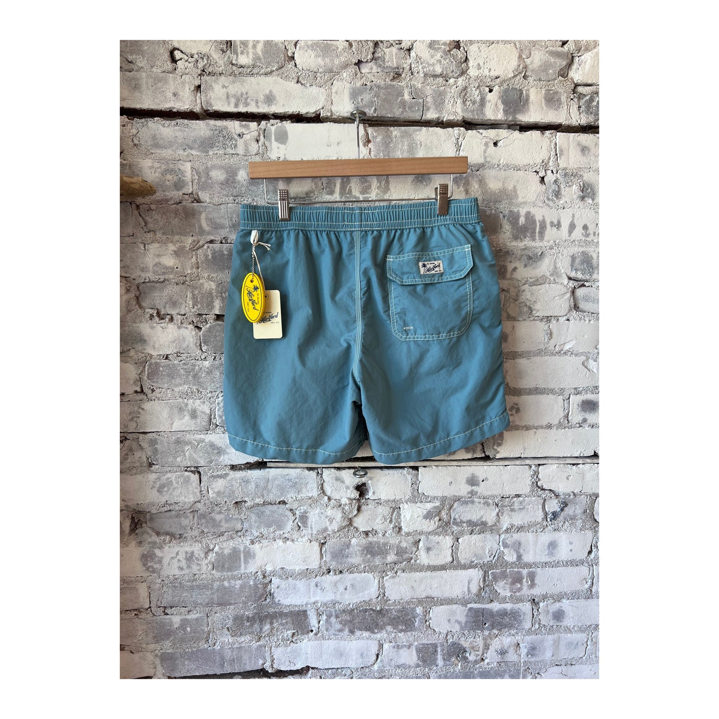 Men's classic swim trunks and sage pochette from Hartford Men's, displayed on a neutral background.
