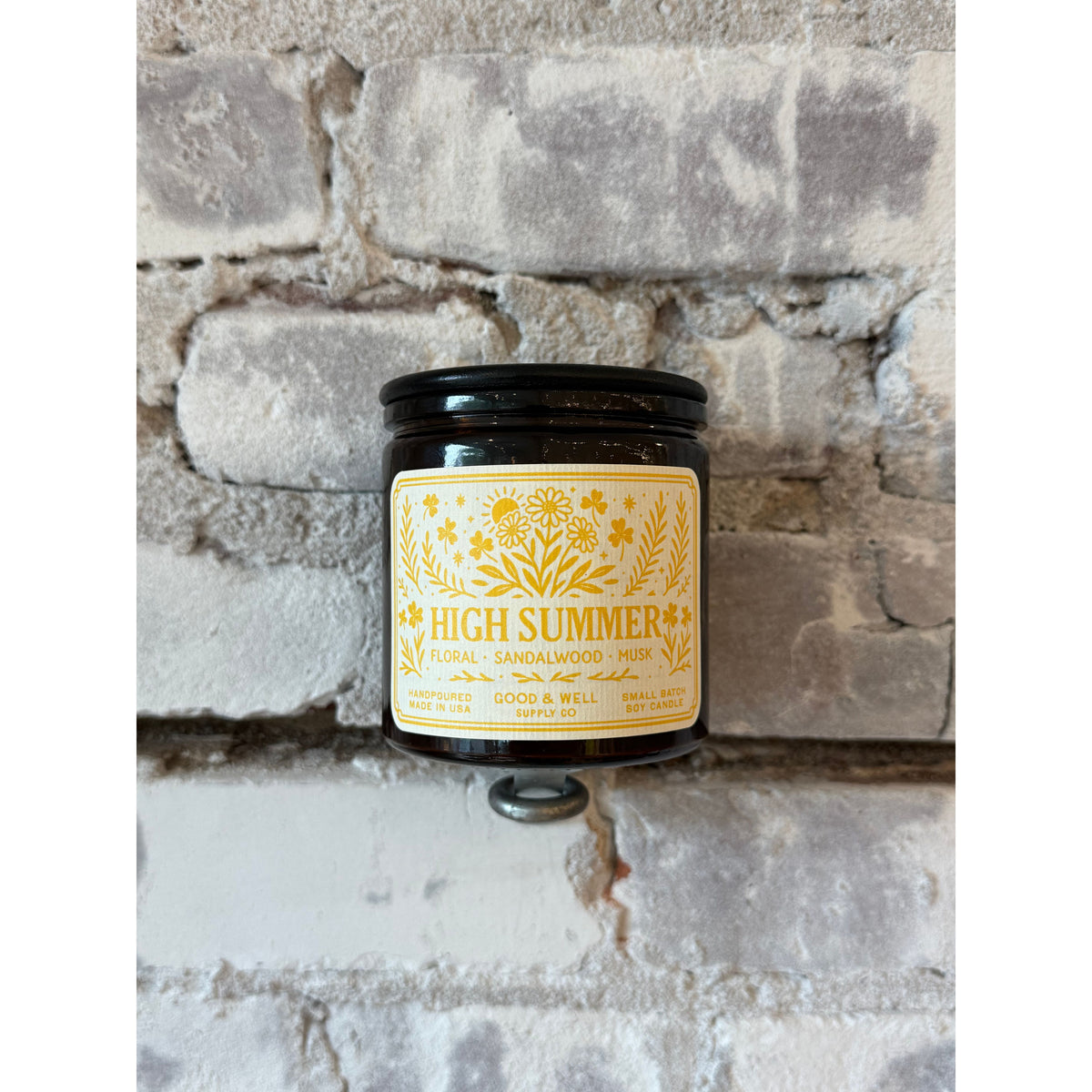 Folk & Flame High Summer Soy Candle in a clear glass jar with a wooden wick, surrounded by summer-themed decor.