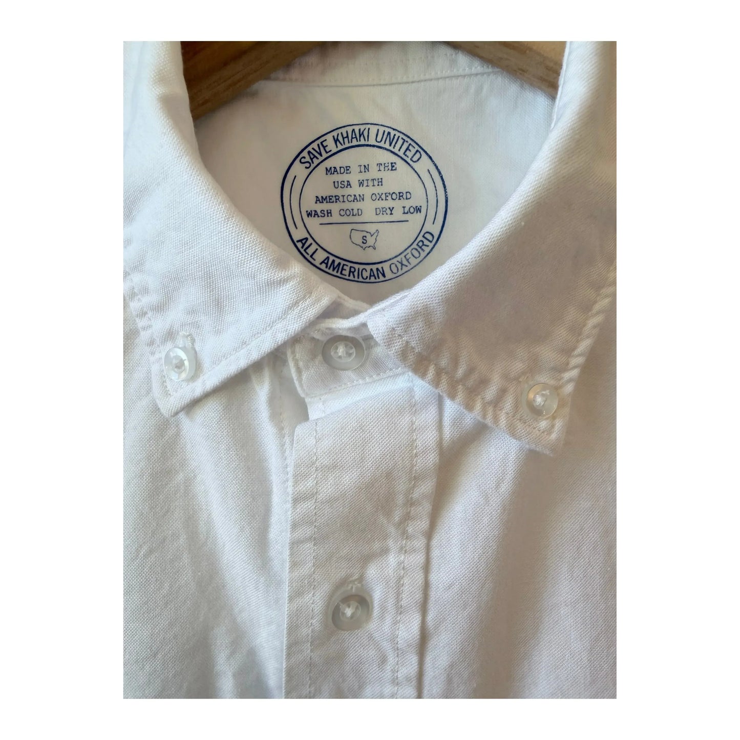 Men's white long-sleeve American Oxford shirt by Save Khaki United, shown hanging on a wooden hanger.