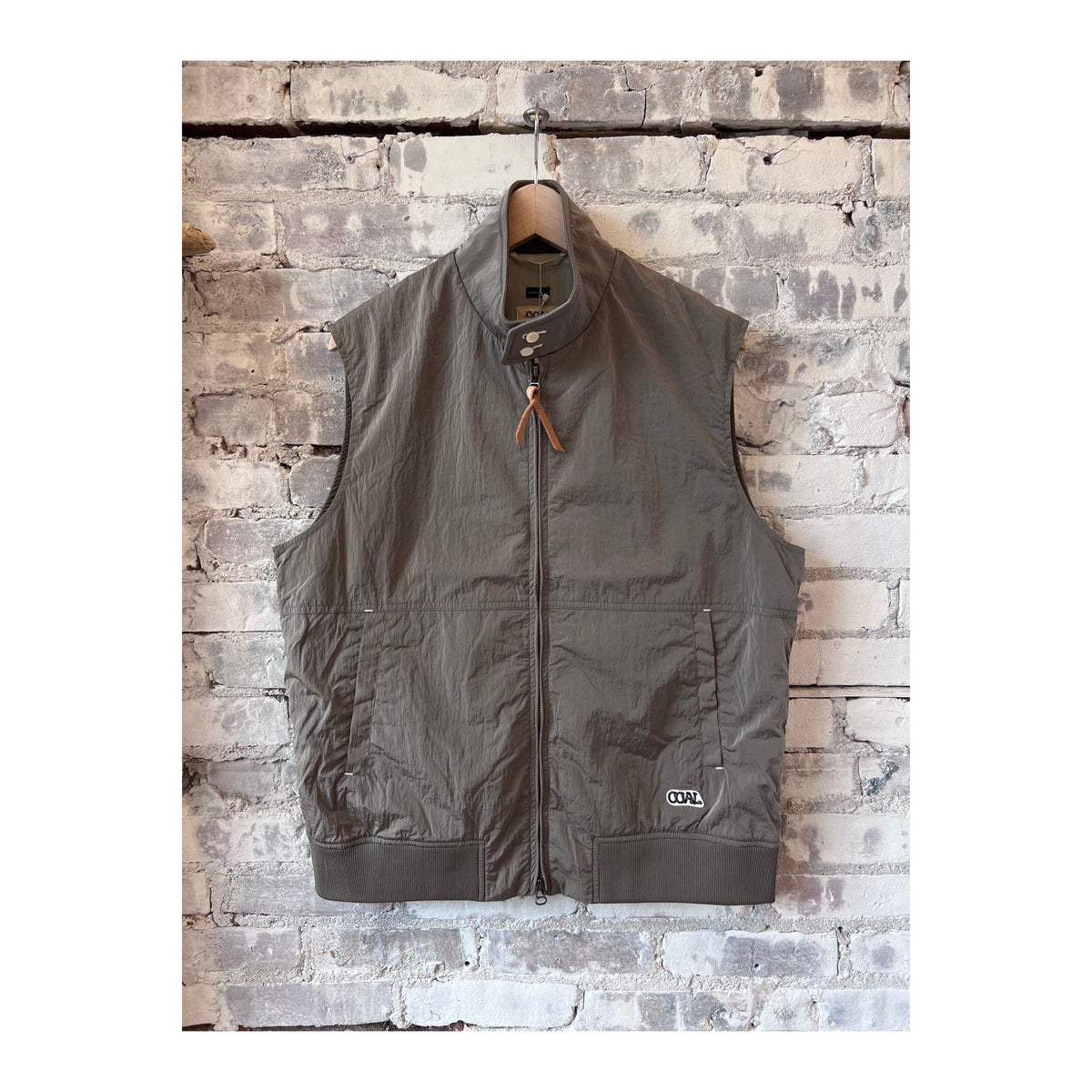 Men's beige nanamica zip-up wind vest hanging on a hanger, lightweight and designed for wind resistance.