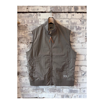 Men's beige nanamica zip-up wind vest hanging on a hanger, lightweight and designed for wind resistance.