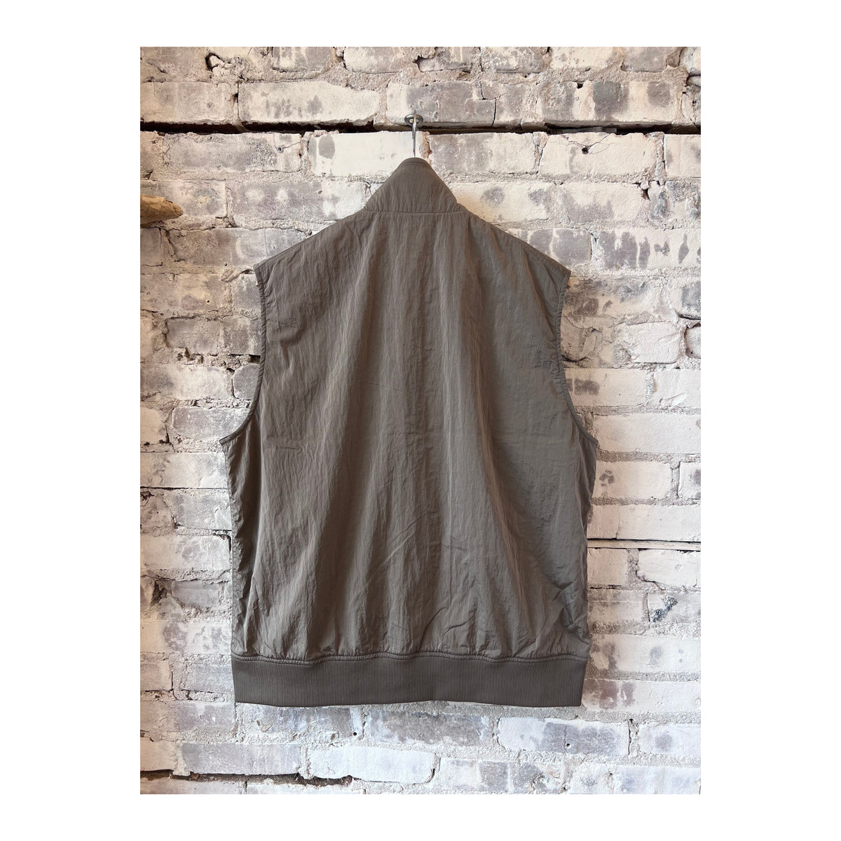 Men's beige nanamica zip-up wind vest, lightweight and weather-resistant, shown on a hanger with a smooth fabric texture.