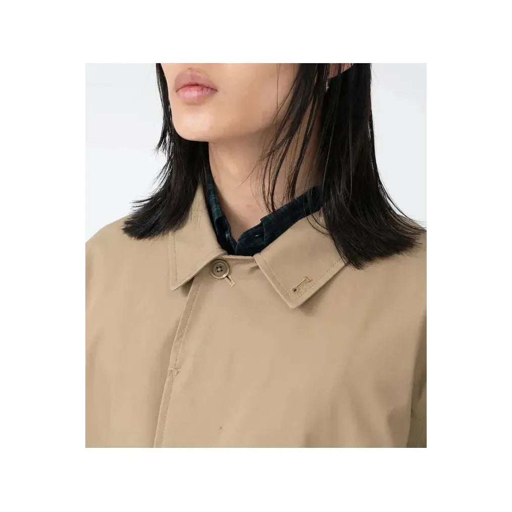 Women's beige nanamica GORE-TEX Soutien Collar Coat hanging on a wooden hanger, showcasing its lightweight, waterproof design and stylish collar.