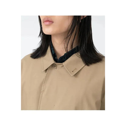 Women's beige nanamica GORE-TEX Soutien Collar Coat hanging on a wooden hanger, showcasing its lightweight, waterproof design and stylish collar.