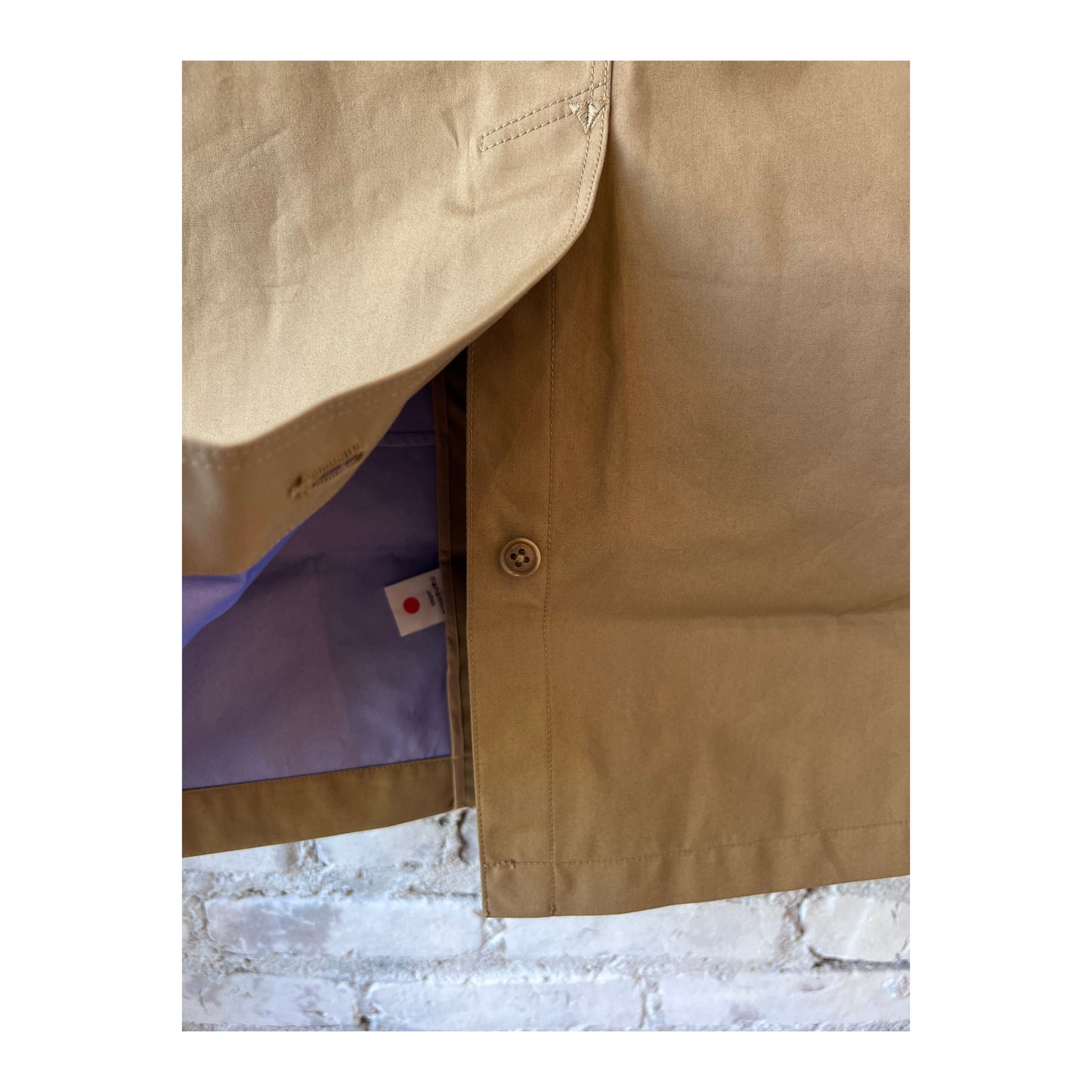 Women's beige nanamica GORE-TEX Soutien Collar Coat displayed on a hanger, showing the collar and sleek fabric texture.