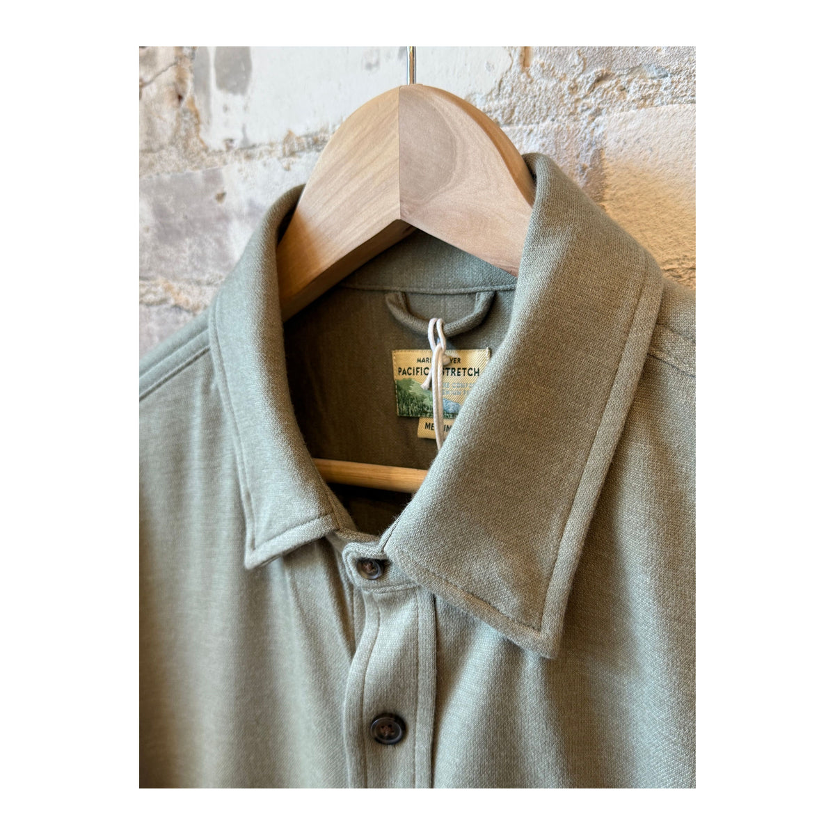 Men's Pacifica Stretch Twill Shirt in Vetiver color, made by Marine Layer, shown on a hanger with a smooth twill fabric texture.