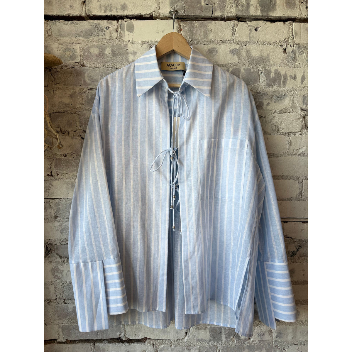 Women's Sicilia Linen Shirt by ACARIA STUDIO in white with blue stripes, shown laid flat with collar and sleeves visible.