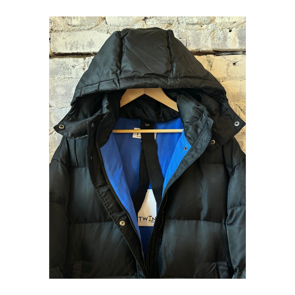 Women's black and royal blue long puffer jacket by TWIN, showing the padded, quilted exterior and hooded design.