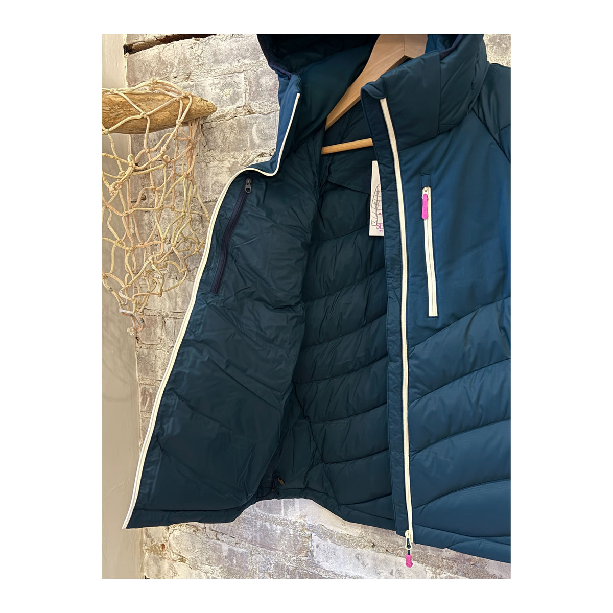 Women's Wildpuff Packable Removable Hood Jacket by Seniq in Slushi color, shown with the hood detached and the jacket folded.