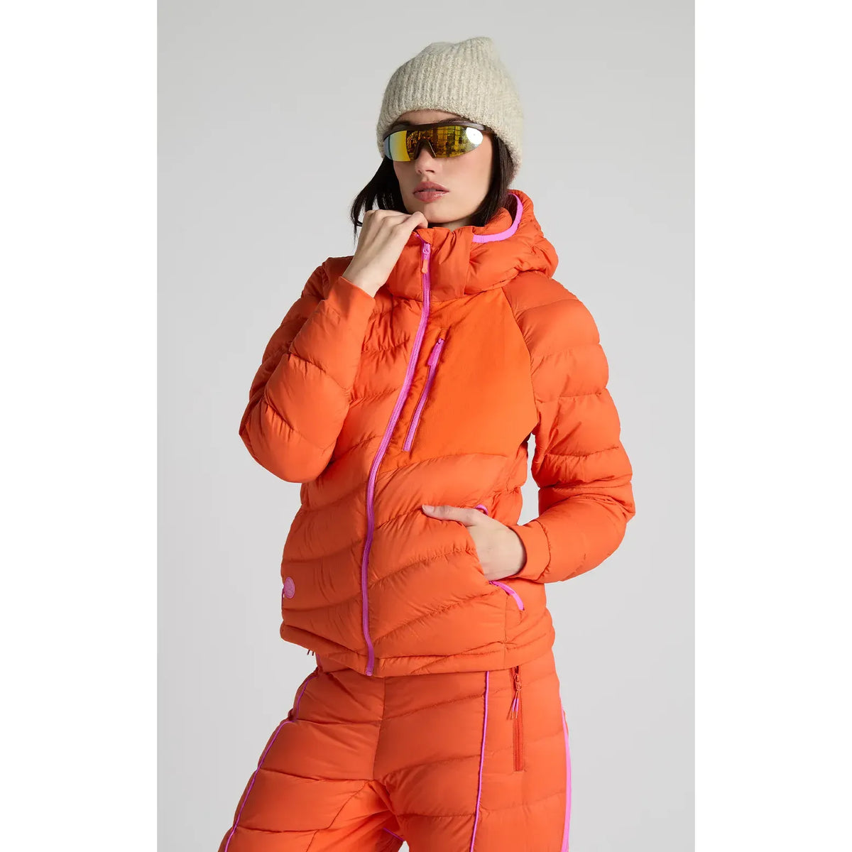 Women's Wildpuff packable jacket by Seniq with a removable hood, in spicy color, shown laid flat with zipper and hood details.