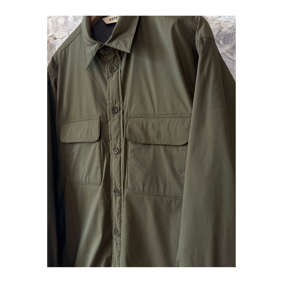 Men's Aspesi Yoshitaka Cotton/Nylon Military Shirt Jacket hanging on a hanger, showcasing its rugged fabric and military-inspired design.